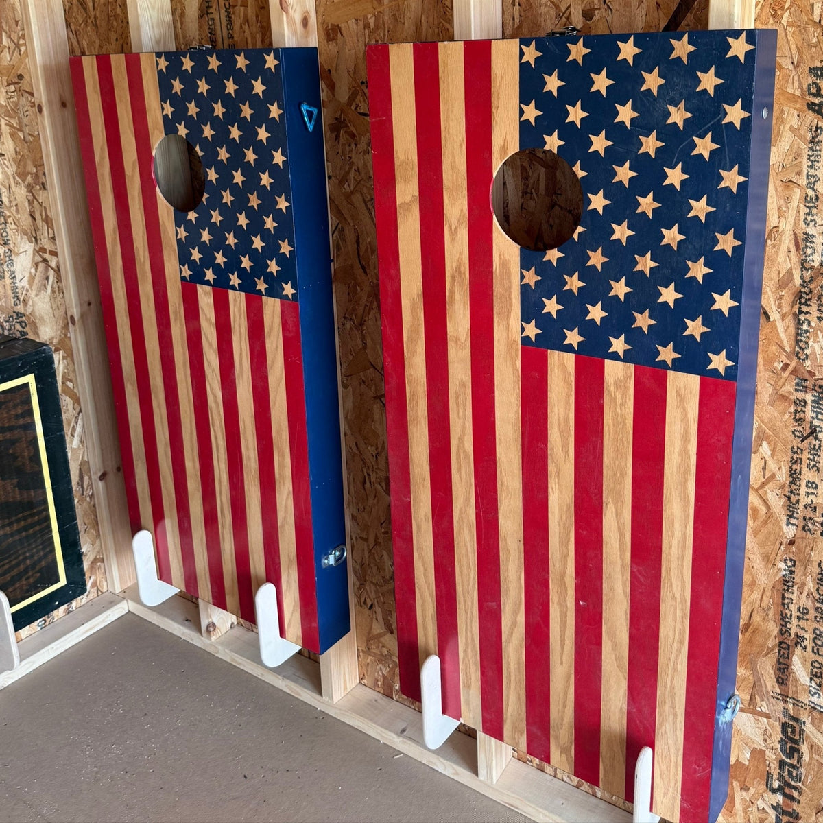 Wall-mounted cornhole board holder installed in a garage holding two cornhole boards