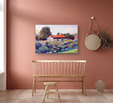 Impressionist painting of a countryside cottage with a red roof surrounded by green and purple foliage against a light blue sky, displayed on a terracotta wall above a wooden bench.