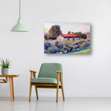 Impressionist-style painting of a countryside cottage with a red roof surrounded by green and purple foliage, displayed above a green chair and wooden table in a minimalist room.