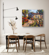 Colorful impressionist painting of a cottage path with vibrant red, yellow, and green foliage, displayed above a modern dining table with wooden chairs and black metal legs.