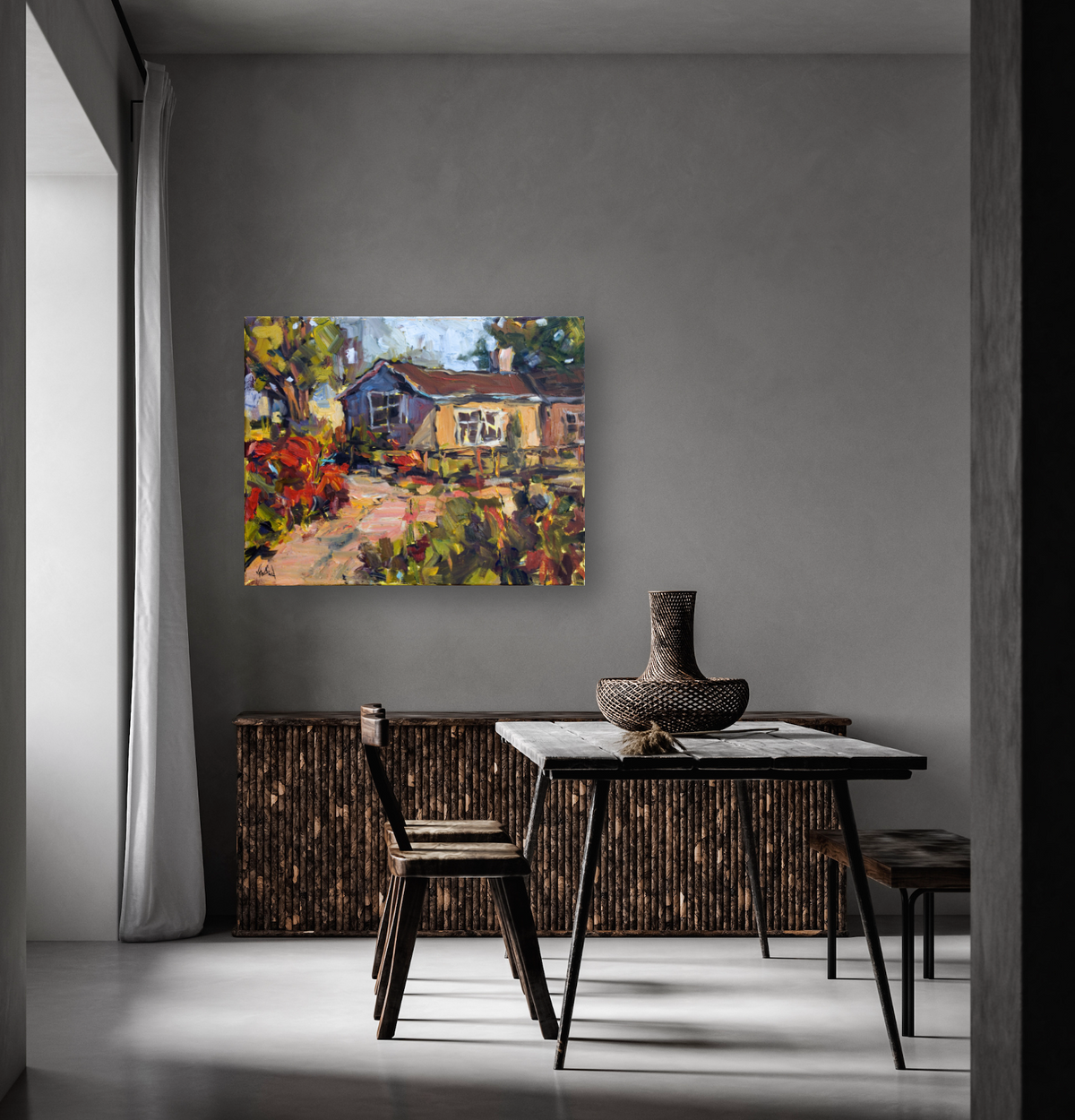 Impressionist canvas painting of a cottage with a tree and colorful foliage, displayed on a gray wall above a rustic dining table with woven pottery.