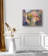 Impressionist canvas painting of a hillside village with cottages in soft purples, greens, and reds hanging on a white wall above a white marble pedestal table with dried floral decor.