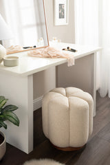 Cream-colored Lucida Round Tufted Ottoman with a wooden base positioned under a white vanity table with a mirror, soft scarf, and makeup brushes on top.