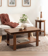 Rectangular wood coffee table with a bottom shelf holding books, placed on a textured beige rug in front of a cream sofa with a rust-colored knit throw.