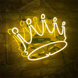 Yellow neon sign shaped as a tilted crown with five rounded points, mounted on a transparent rectangular panel against a textured brick wall.