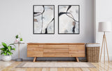 Minimalist living room with abstract black and white canvas art above a wooden low credenza, flanked by a small plant table and a wicker basket with a cushion.