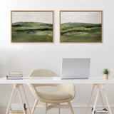 Two framed canvas paintings of green rolling hills with dark and light green brushstrokes, hung side by side above a white desk with a beige chair and a laptop.