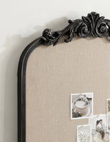 Close-up of an ornate black arch-shaped frame with intricate scrollwork and a beige fabric pinboard holding small photos and printed images.