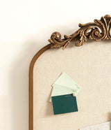 Close-up of an ornate golden wood frame arch with fabric pinboard displaying three attached green color swatches, set against a white wall background.