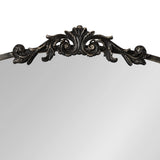 Close-up of ornate black metal scrollwork with symmetrical leaf and curl motifs atop an arched mirror frame.