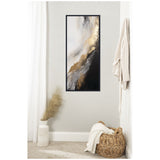 Vertical abstract canvas with flowing gold, black, gray, and white swirls, framed in black, hanging on a light wall above a wicker basket and a white vase with pampas grass.