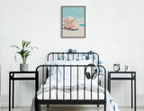 Framed canvas print above a black metal bed, showing a pink van on a sandy beach with a clear blue sky, decorated with blue and gray lights around the bed frame.
