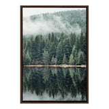 Framed canvas of dense evergreen forest with mist above and clear reflection in calm lake below, emphasizing tranquility and natural symmetry.