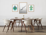 Dining room with wooden table and six beige chairs under three framed artworks: teal sea turtle, black-and-white flying bird, and stylized green shellfish on white wall.
