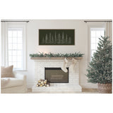 Minimalist living room with white brick fireplace decorated with garland, two beige stockings, a large green Christmas tree, and framed Sylvie evergreen tree sketch above fireplace.