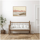 Framed abstract wall art depicting layered hills in brown, beige, and cream tones above a wooden bench with white cushions in a bright minimalist room.