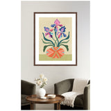 Framed abstract floral artwork featuring purple and pink irises with green leaves in an orange geometric-patterned vase on a light beige and green background, hanging above a cozy armchair and round wooden table.