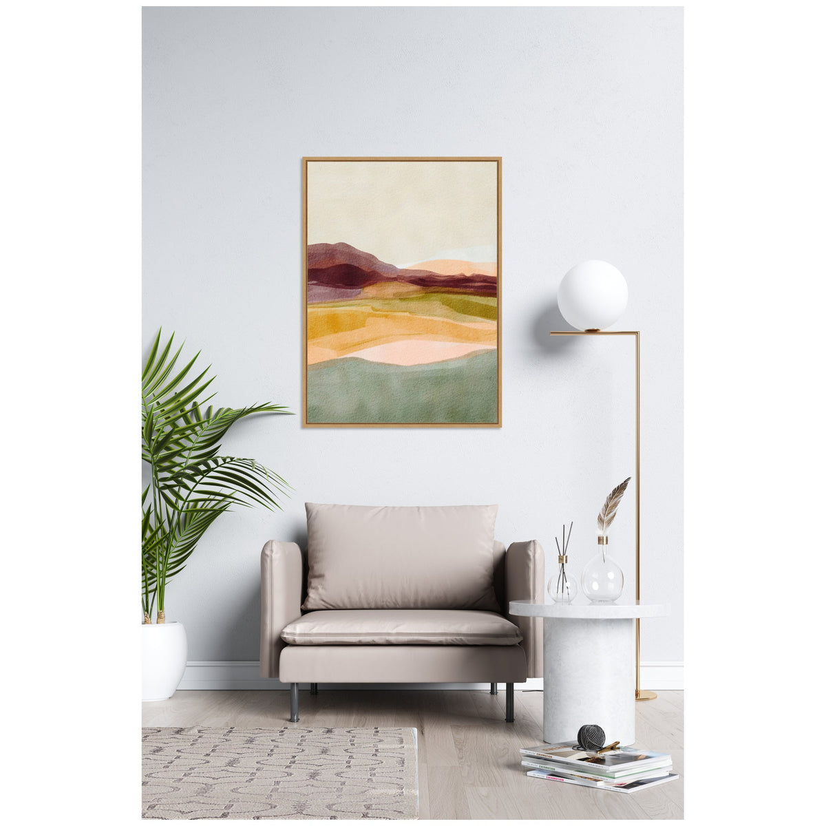 Abstract landscape painting with layers of muted maroon, yellow, peach, and green hues in a simple wooden frame above a beige armchair in a minimalist white room.
