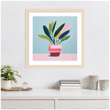 Framed colorful painting of a potted plant with bold green, blue, pink, and yellow leaves on a pale blue and pink background, hanging above a white dresser.