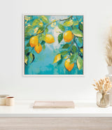 Framed painting of a lemon tree branch with ripe yellow lemons and green leaves against a blue background, hanging on a white wall above a white shelf.