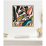 Square framed canvas print of abstract botanical shapes with bold outlines in teal, orange, mustard, green, and brown on a pale pink background, hung on a white wall above a desk with neutral decor.