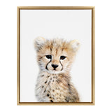 Portrait of a young cheetah with large dark eyes and spotted fur, set against a plain white background in a simple wooden frame.
