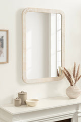 Rectangular wall mirror with rounded corners and a light wood textured frame, mounted above a white mantle featuring neutral ceramic vases and dried grass decor.
