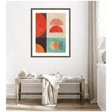 Framed abstract wall art with red, orange, black, and teal semi-circles arranged in a grid on a light textured background, hung above a rustic wooden bench.