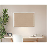 Rectangular cork pinboard with a white scalloped border framed in white, mounted on a beige wall above a modern desk with books and a plant to the left.