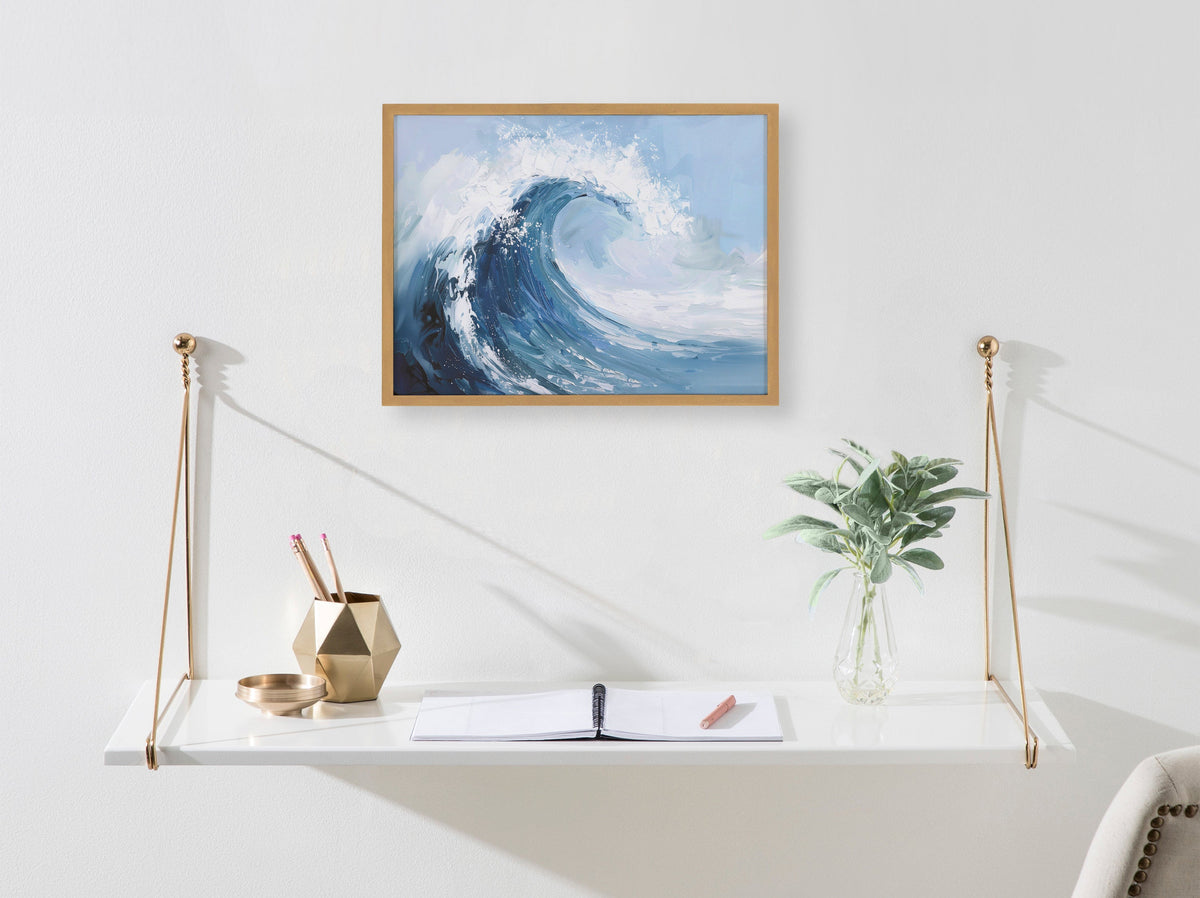 Painterly abstract print of a curling ocean wave in blue and white tones, framed and hung above a white floating desk with gold accents and a green plant.