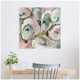 Framed painting of oyster shells in soft pastel hues of pink, blue, and green with subtle shadows on a neutral background, hanging above a wooden desk with a plant.
