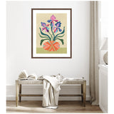 Framed colorful abstract iris flowers in a patterned round vase hanging above a woven wooden bench with a draped white cloth and open book in a light, airy room.
