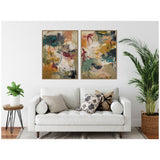 Two abstract framed canvas paintings with green, yellow, beige, and red tones hang above a white sofa adorned with patterned and solid pillows, flanked by plants.