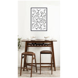 Minimalist black line drawing of various wine glasses on white background in a black frame above a wooden bar table with two matching stools and ceramic cups.