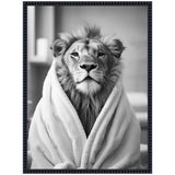 Black and white portrait of a lion wrapped in a soft, textured towel with a blurred interior background, framed in a decorative black frame.