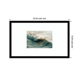 Framed wall art print featuring a photograph of a wave breaking with soft morning light illuminating the crest and a surfer riding it, set in a black rectangular frame.