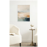 Abstract coastal wall art with soft blue, beige, and burnt orange tones above a brass side table with a white vase and two cream upholstered chairs in a neutral room.
