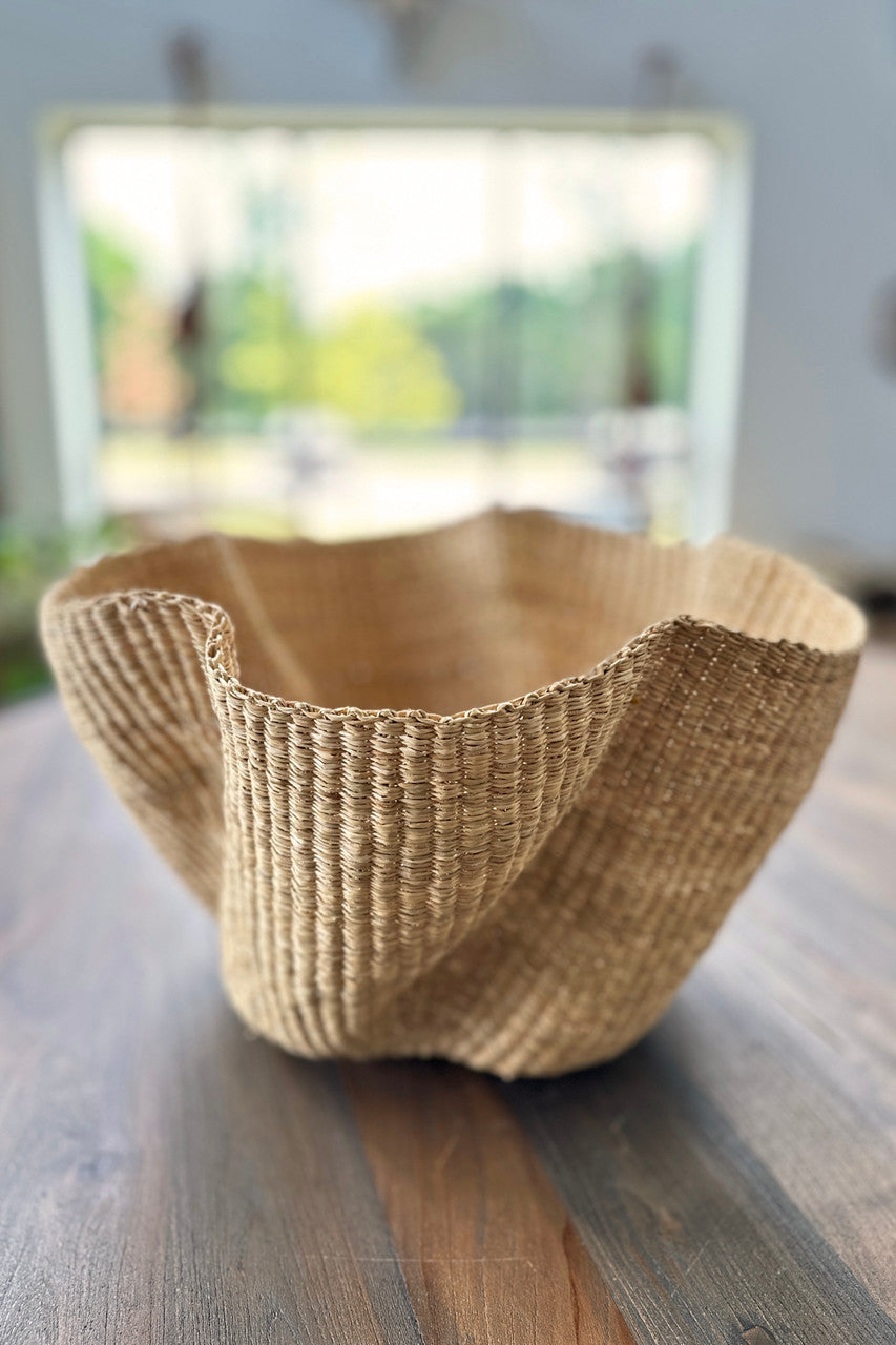 Natural Wave woven basket with undulating pattern made of undyed elephant grass, displayed in a minimalist room