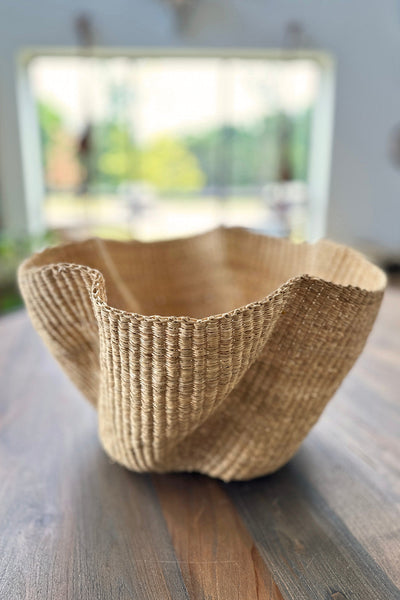 Natural Wave woven basket with undulating pattern made of undyed elephant grass, displayed in a minimalist room