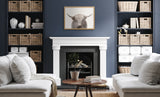 Modern living room with white sofas, navy blue built-in shelves holding wicker baskets and books, and a framed Highland cow print above a white fireplace.