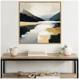 Abstract landscape painting with layered mountain shapes in dark green and blue tones overlooking a reflective lake in beige and light gray, framed in light wood and hung above a wooden console with neutral decor.