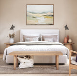 Neutral-toned bedroom with a white upholstered bed, wooden bench, matching nightstands with modern gray lamps, and an abstract landscape painting above the bed.