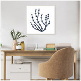 White-framed canvas with a black-blue botanical coral seaweed print hanging above a minimalist wooden desk with a beige upholstered chair and potted plants nearby.
