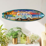Oval surfboard-shaped wall art depicting a blue and white vintage van with dolphin decals parked on a sandy beach at sunset, framed by palm trees and ocean waves.
