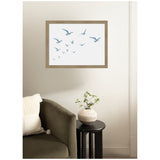 Minimalist framed wall art of blue seagulls in flight on a white background hanging above an olive green sofa and black round side table with a beige textured vase holding green foliage.