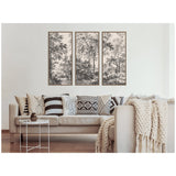 Three-panel framed black and white canvas wall art depicting detailed wooded trees above a beige sofa adorned with patterned black and white pillows and a chunky cream knit throw.