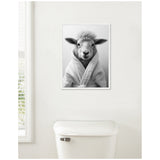 Black and white framed canvas of a sheep wearing a robe, hanging on a white wall above a white toilet in a bathroom setting.