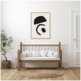 Minimalist living room with wooden bench seating white cushions, a round braided rug, and abstract black shapes artwork in a natural wood frame on white wall.