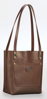 Tall brown leather tote bag with long narrow shoulder straps and a front pocket embossed with a circular logo, against a plain white background.