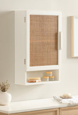 White wall-mounted cabinet with a woven rattan door panel and an open cubby below holding wooden brushes and jars, set against a light beige wall.